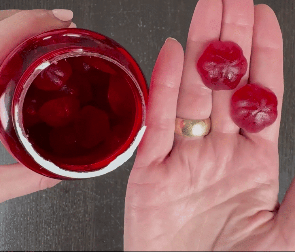 Hand holding two Goli apple cider vinegar gummies next to a jar of gummies.